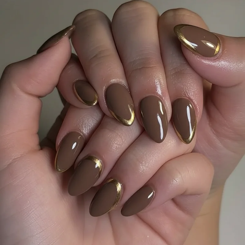 Gold chrome diagonal French tip on mocha base almond nails for graphic modern metallic manicure design 2026