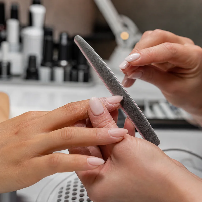 Nail technician filing almond shape showing proper tapering technique on both sides of nail during first salon appointment for beginner client