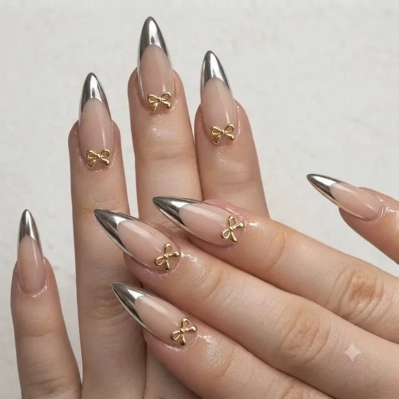 Chrome French tip nails with a small gold bow charm placed at the base near the cuticle