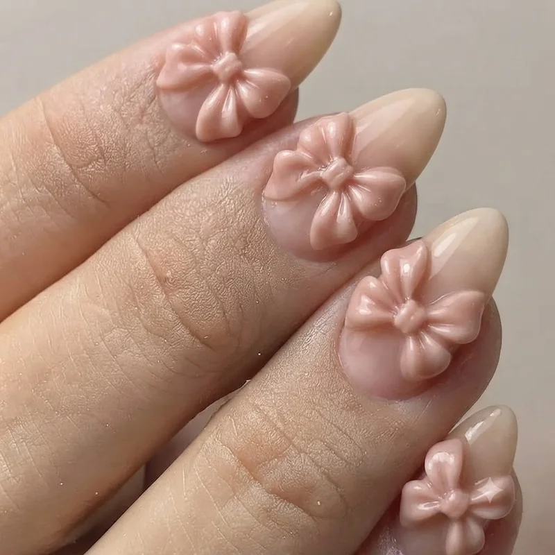 Dramatic long almond nail with a large sculpted 3D bow shown in editorial statement styling