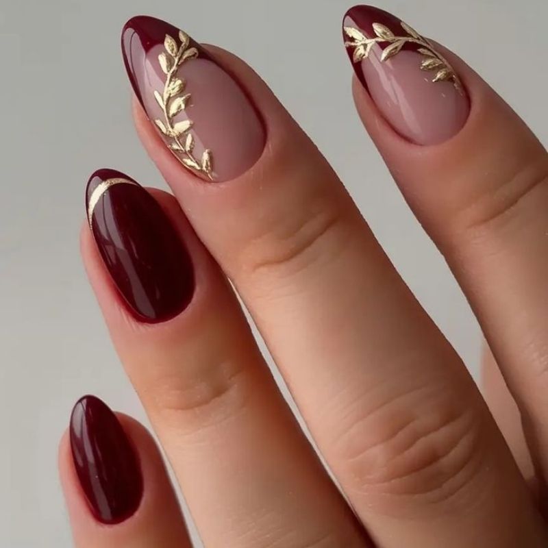elegant burgundy and emerald green christmas nails with gold leaf accents on almond shaped nails