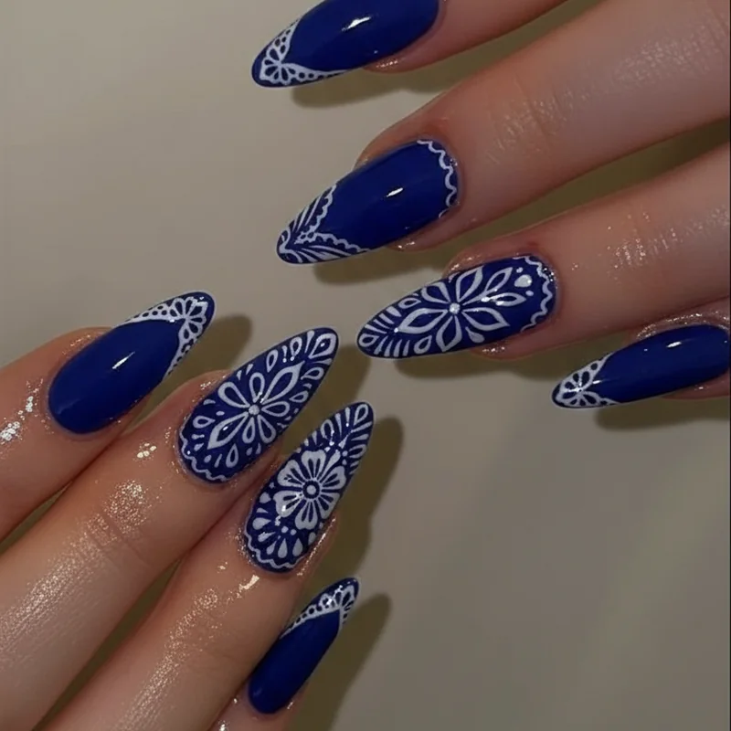 Papel picado nail art showing white linework floral and geometric border pattern on deep cobalt blue base inspired by Mexican cut paper folk art