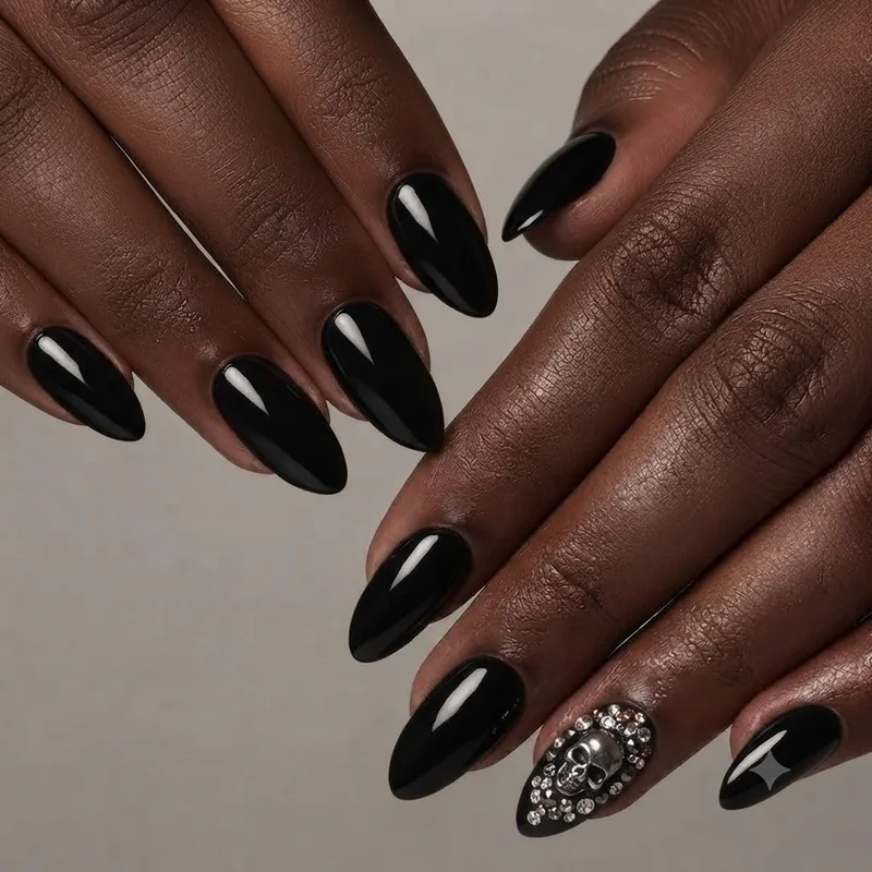 Black halloween nails in stiletto shape with 3D skull charm and scattered rhinestone accents