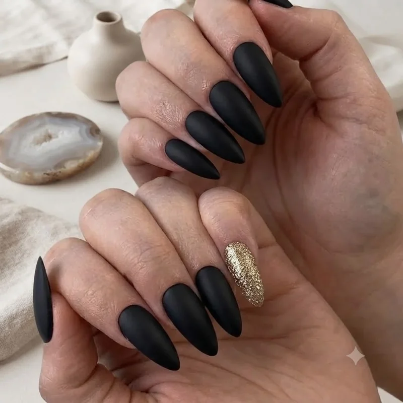 Matte black Halloween nails at home with one gold glitter accent nail, easy beginner manicure finished at a kitchen table
