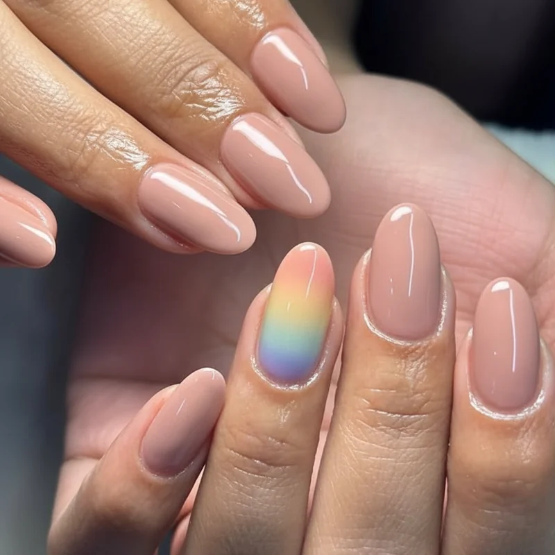 Single accent pride nail design showing intentional ring finger muted flag ombre against four nude base nails for cohesive minimalist manicure