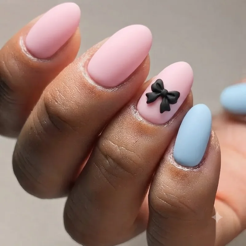 Cry Baby era Melanie Martinez nail art with pastel pink and baby blue base, black bow accent and matte doll-like finish
