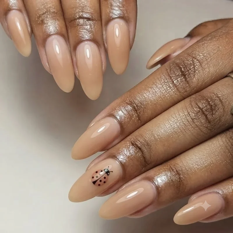 Soft nude and honey toned manicure with a single hand painted ladybug accent nail, a folk aesthetic styling choice