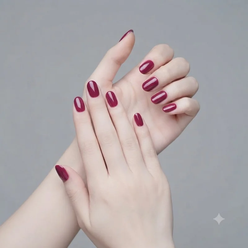 Dark nail polish for fair skin: glossy deep berry short nails on a pale hand in soft window light, quiet neutral backdrop