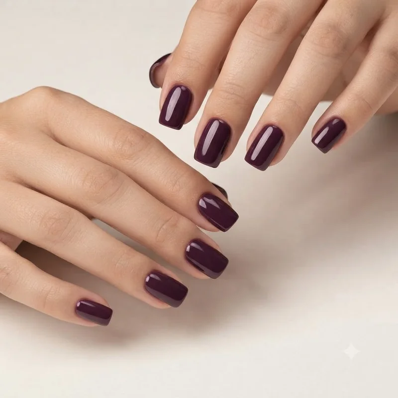 Short squoval nails in glossy dark plum showing a flat tip, softened corners, straight sidewalls, and a clean cuticle line
