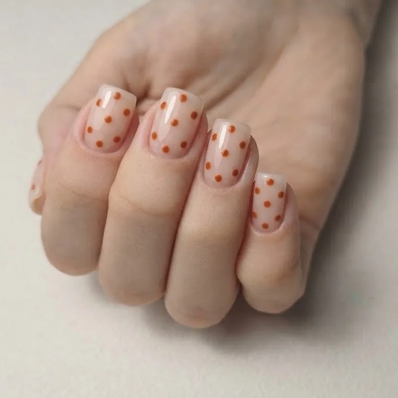 Short square october nails featuring negative space design and burnt orange polka dots