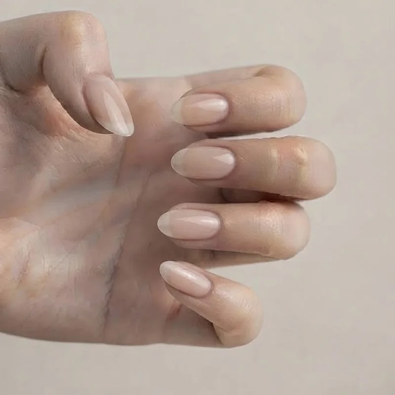 Close-up of medium-length oval nails in sheer neutral polish showing the fully rounded tapered tip