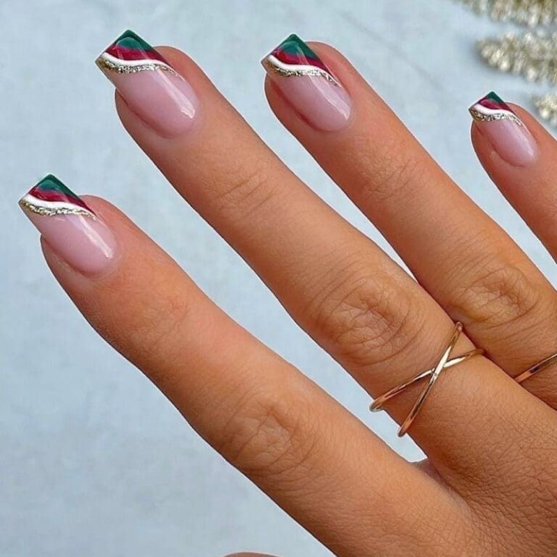 alternating red and green french tip christmas nails with gold line accent on nude base