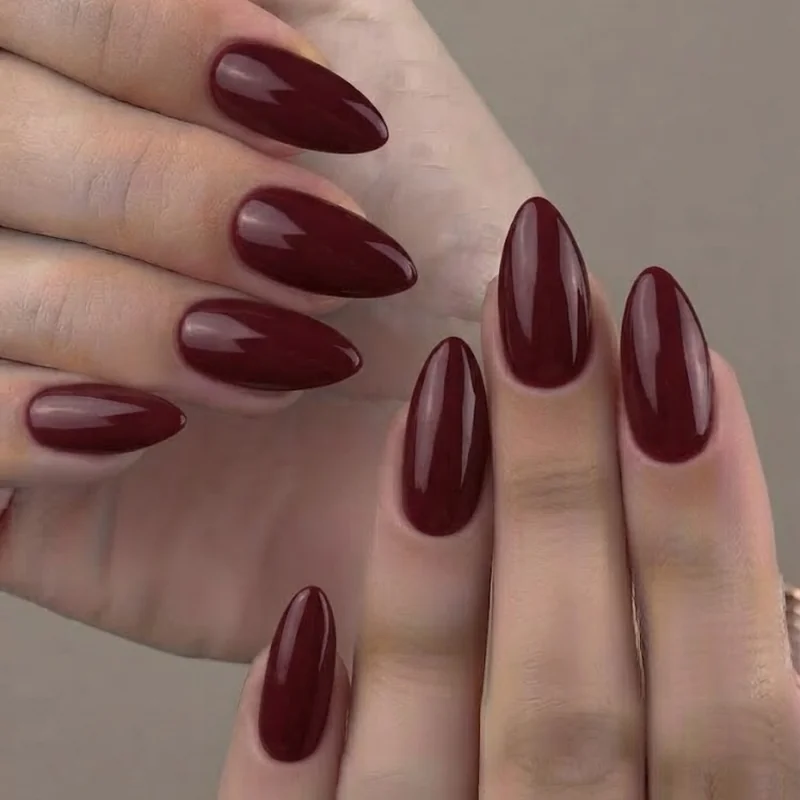 Medium-length almond nail shape manicure shown in a deep burgundy fall polish shade with an elongated tapered pointed tip