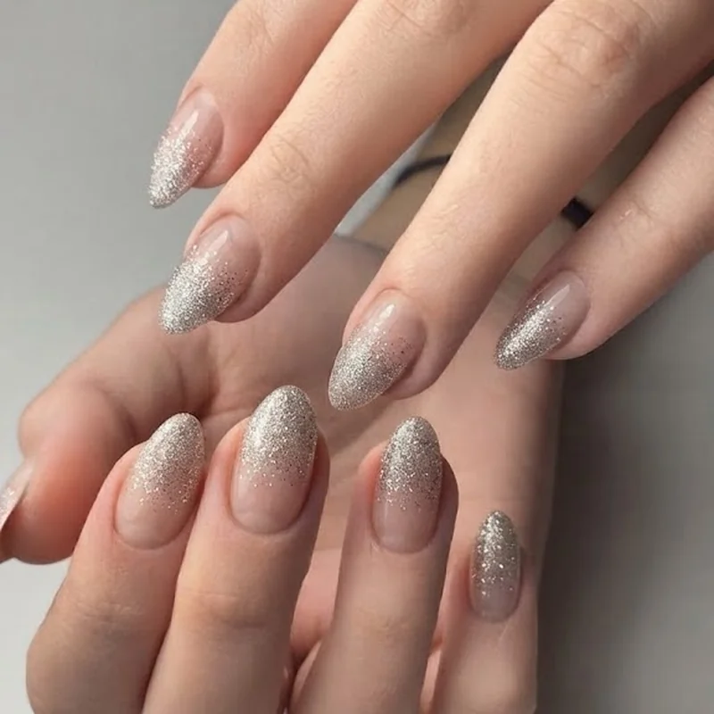 Fine silver glitter ombre on almond nails fading from tip to bare base near cuticle