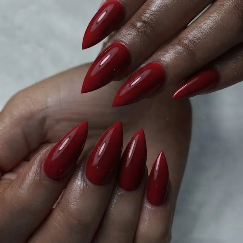 Blue-based cherry red stiletto nails with glossy finish showing high contrast on deep skin tone