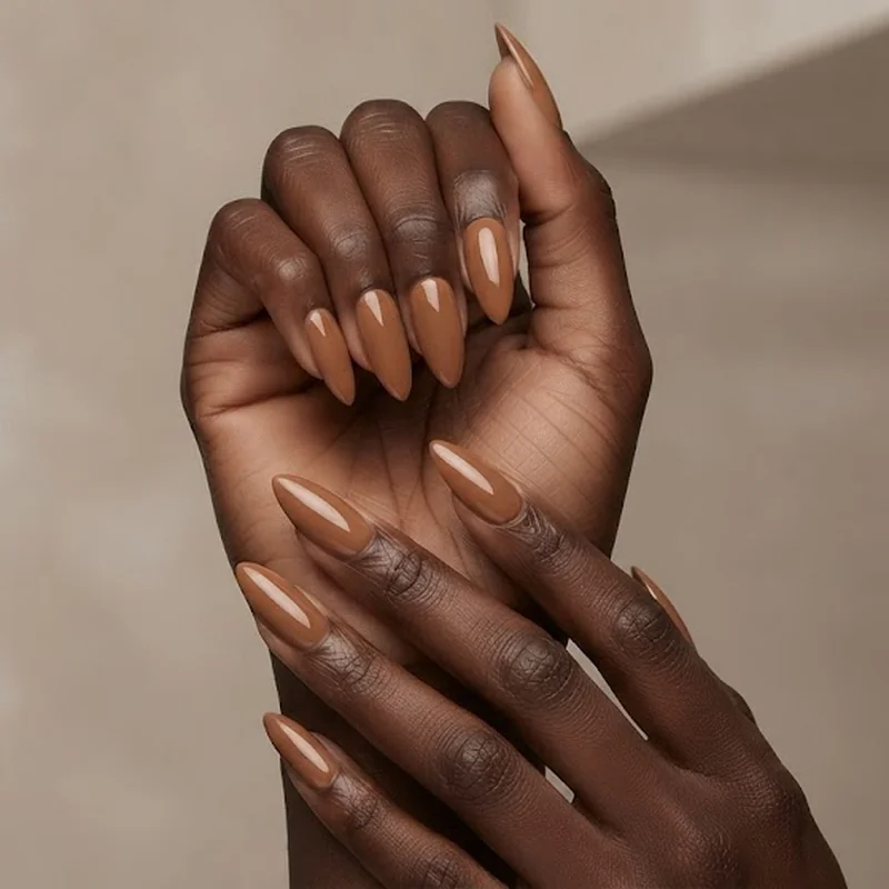 Deep caramel butterscotch nude stiletto nails in natural lighting showing skin-matched effect on dark skin