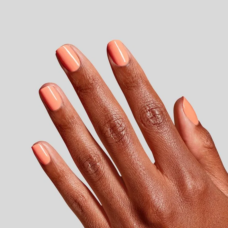 Warm coral and peach nail polish shades on mature hands showing flattering anti-aging effect with natural lighting