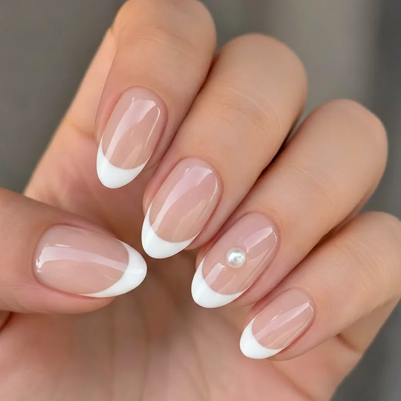 Pearl French tip wedding nails with a single pearl placed at cuticle of ring finger accent nail on sheer pink micro French