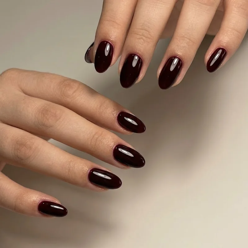 Glossy deep burgundy gel nails in a short almond shape catching warm window light, a rich winter gel manicure color idea