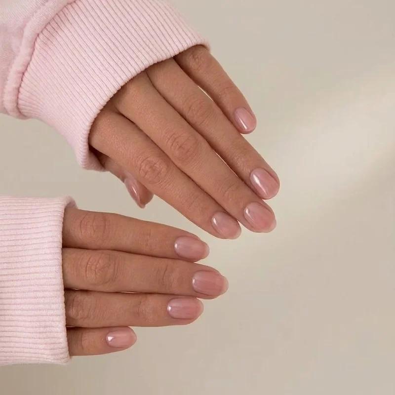 Glossy sheer pink gel nails resting on soft fabric, a short natural shape gel manicure that suits a hydrated winter nail