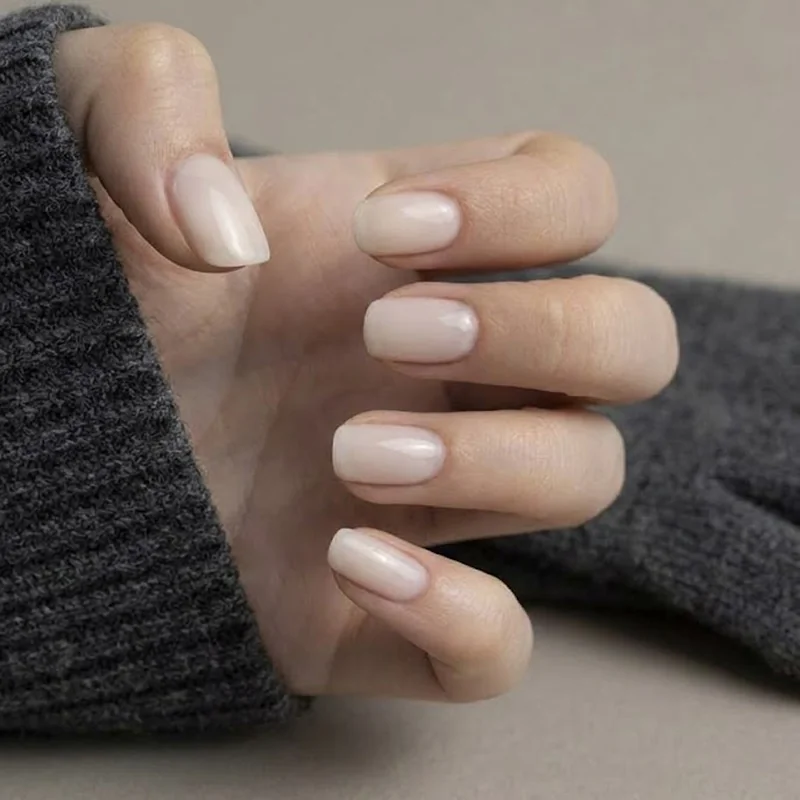 Milky neutral gel nails at a short natural length beside a gray wool glove cuff, showing gloves and gel nails in cold weather