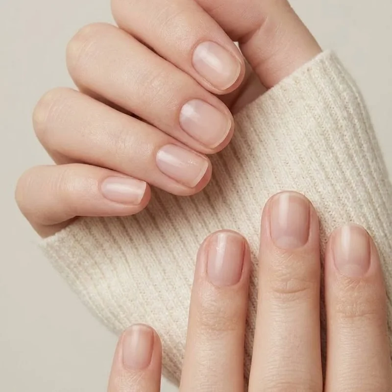 Short natural nails in soft winter light resting on a cream knit sleeve, showing a healthy nail growth rate in cold weather