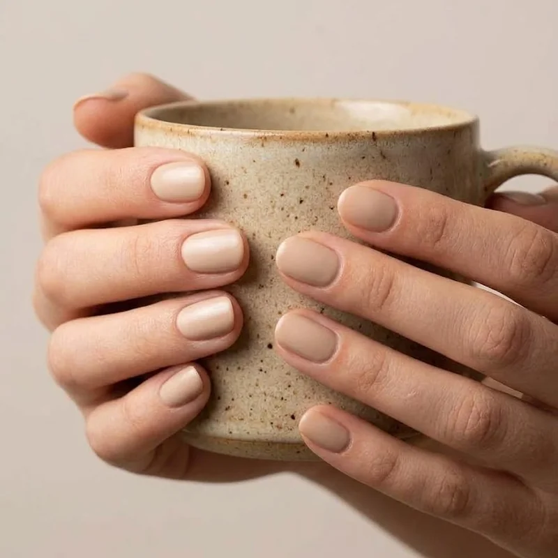 Hands cupping a warm mug with short rounded nails and soft neutral polish, a simple way to keep fingers warm in cold weather