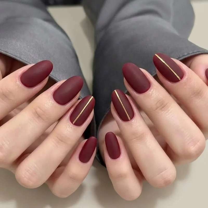 Matte winter nail design with thin gold hairline accent detail over burgundy base