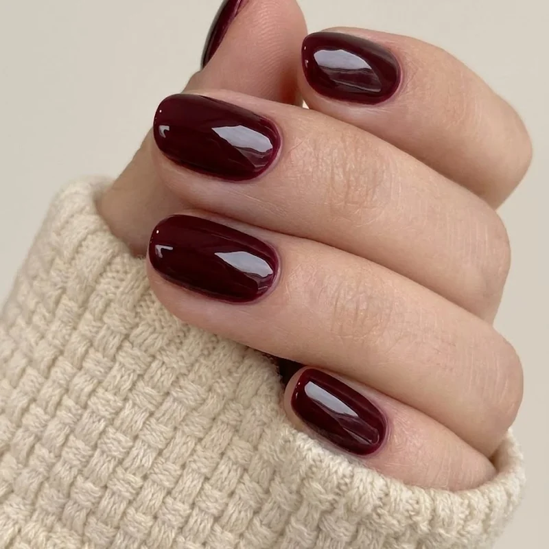 Short winter nails in a glossy cherry burgundy deep red polish, finished with a high-shine winter topcoat look overall