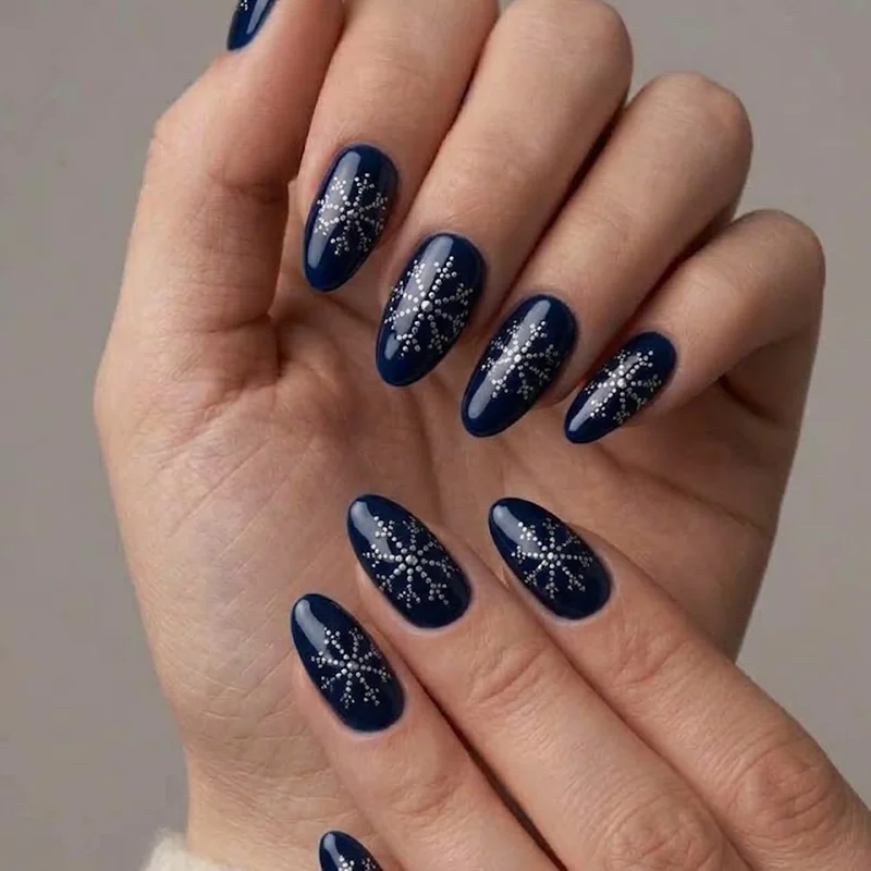 Dotted snowflake nail design in silver polish over a deep navy winter manicure base