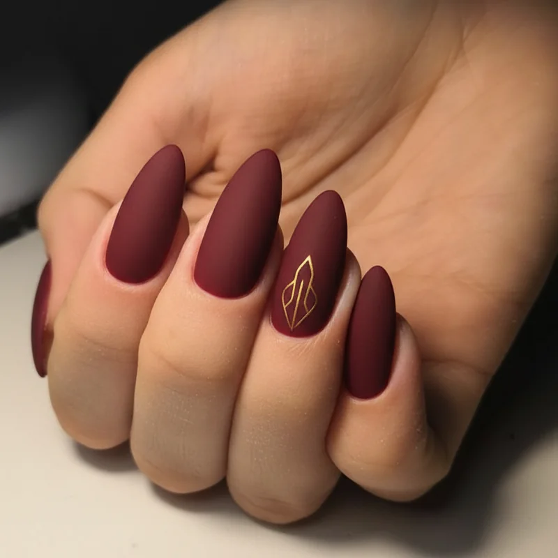 Work-appropriate Aries nails in burgundy deep red matte finish with single gold accent nail for professional office settings