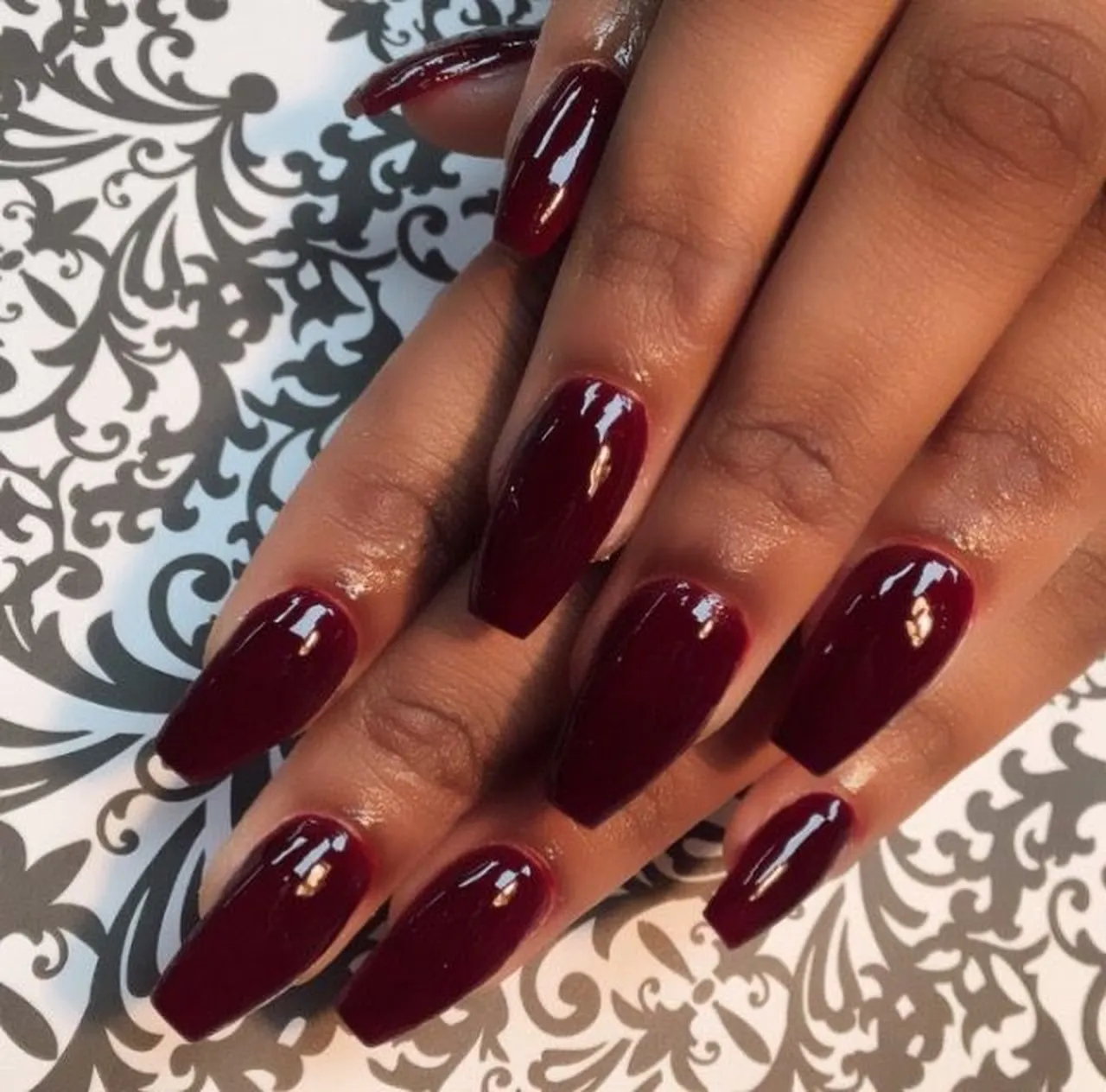 Wine red glossy coffin nails with high shine burgundy finish creating statement winter manicure perfect for elegant party events