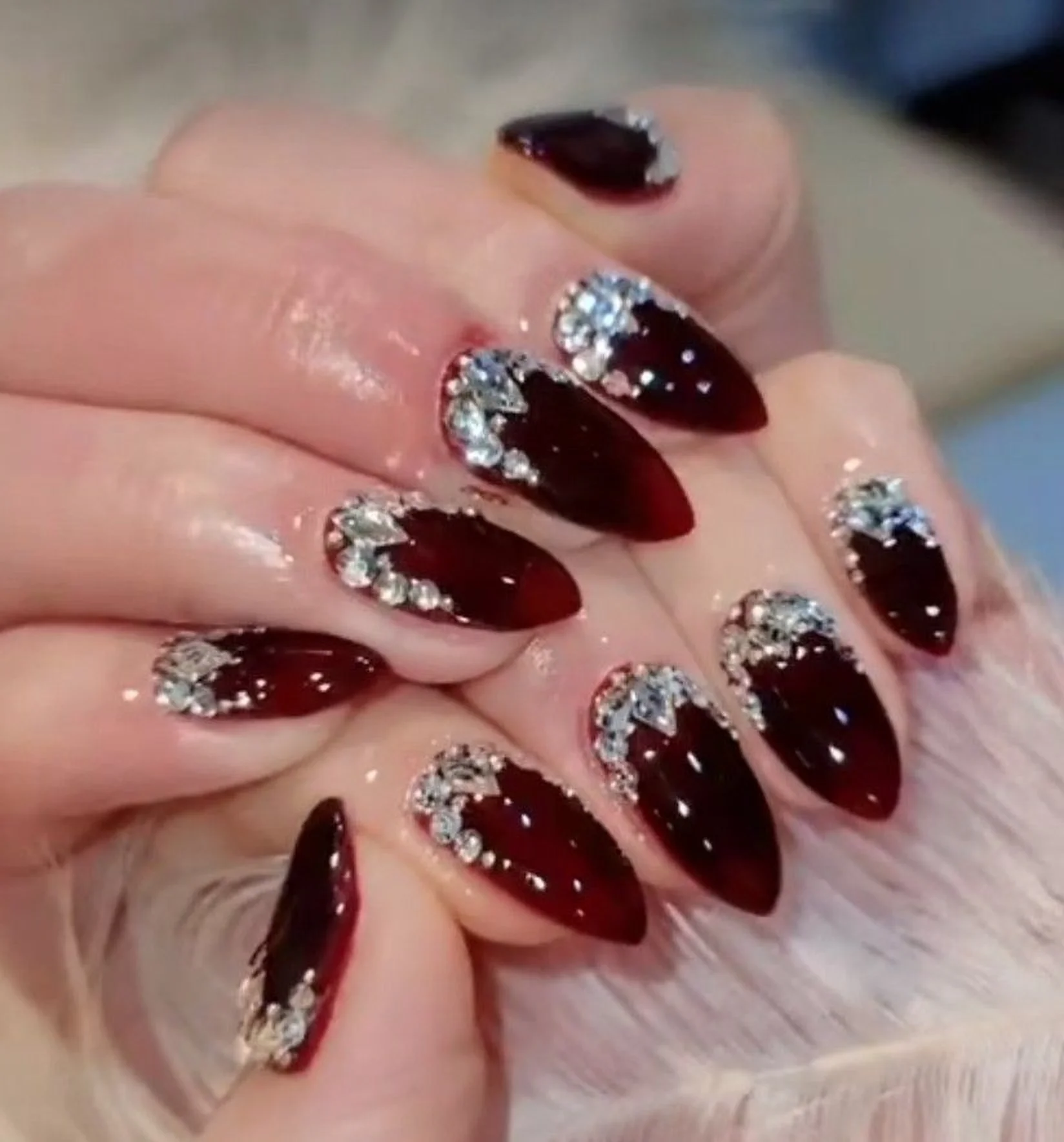 Wine red nails with rhinestone accent creating luxury gem burgundy winter manicure design perfect for glamorous holiday party style