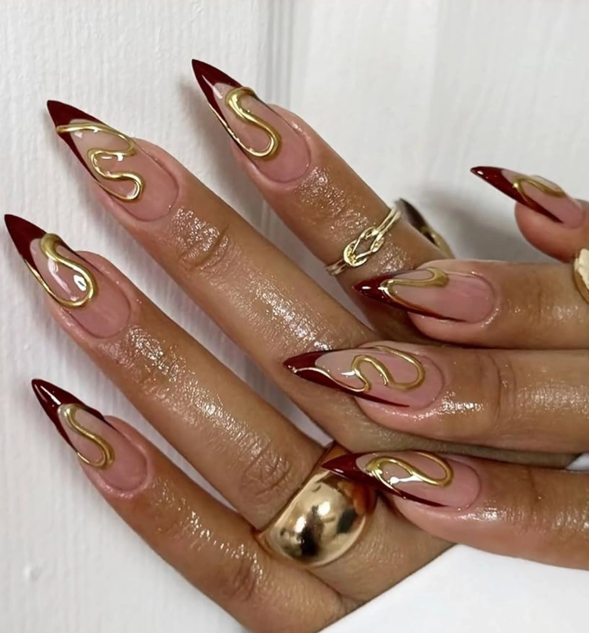Gold chrome accent nails over burgundy base creating luxury winter party manicure with metallic foil details for holidays