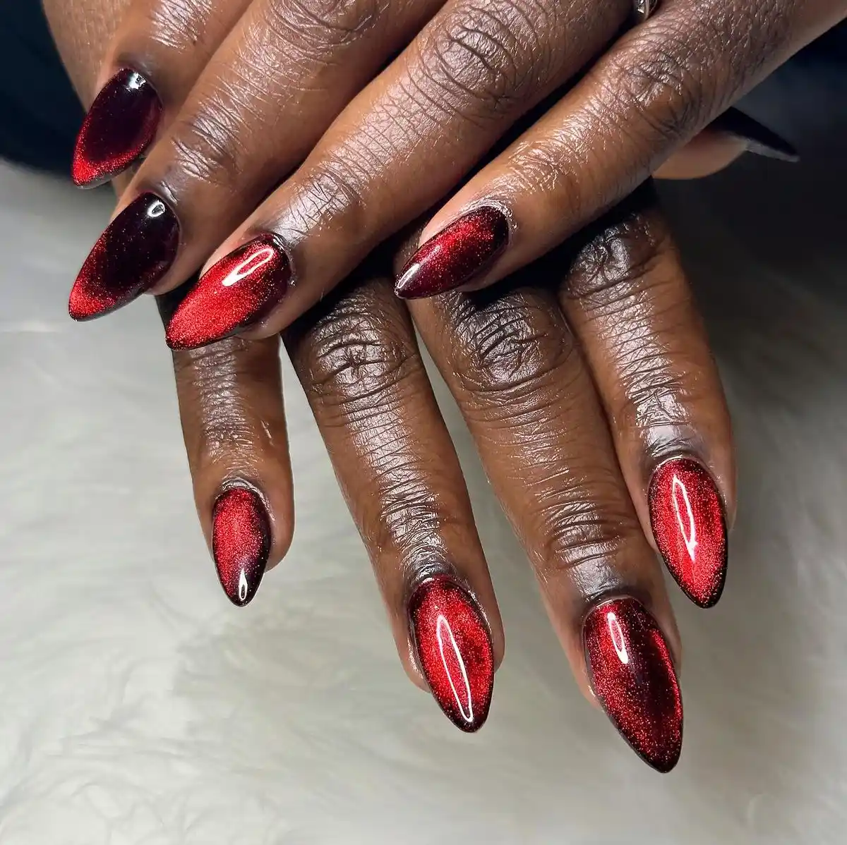 Ruby red velvet almond nails with cat eye magnetic finish creating luxe winter manicure design perfect for romantic elegant style